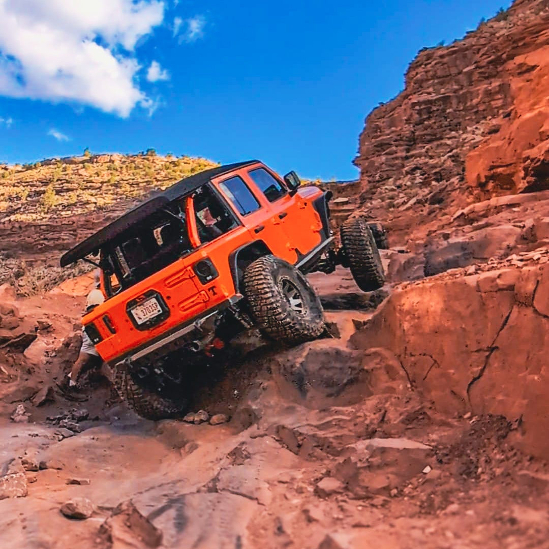 Orange off-road vehicle navigating a rocky desert landscape with a clear blue sky.
