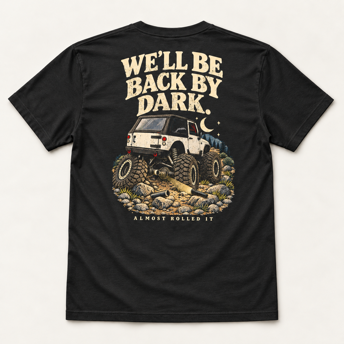 Back By Dark tee in Vintage Black, back flat lay showing We'll Be Back By Dark above a lifted white rig, moon and broken driveshaft pieces.
