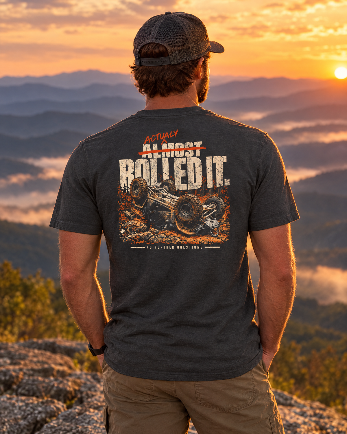 Man wearing the Actually Rolled It tee on a mountain ledge at sunset, back print showing