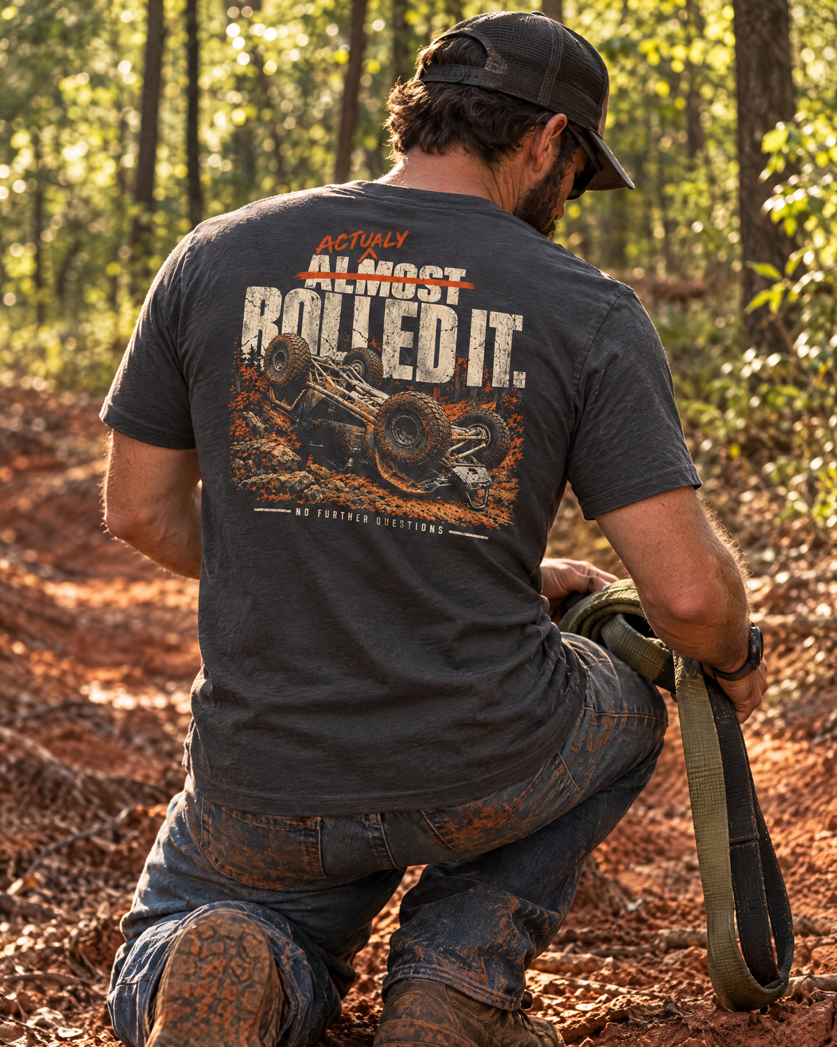 Man kneeling on a red-clay trail in the Actually Rolled It tee