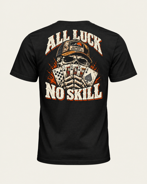 All Luck No Skill tee in vintage black, back view: skull in a trucker cap holding a royal flush of spades, cream and orange lettering