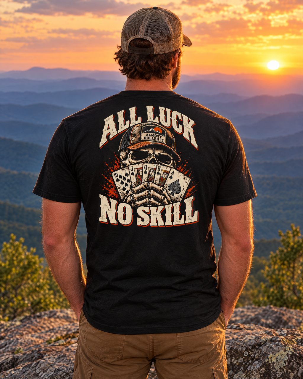 Man wearing the All Luck No Skill tee on a mountain ledge at sunset, back print showing