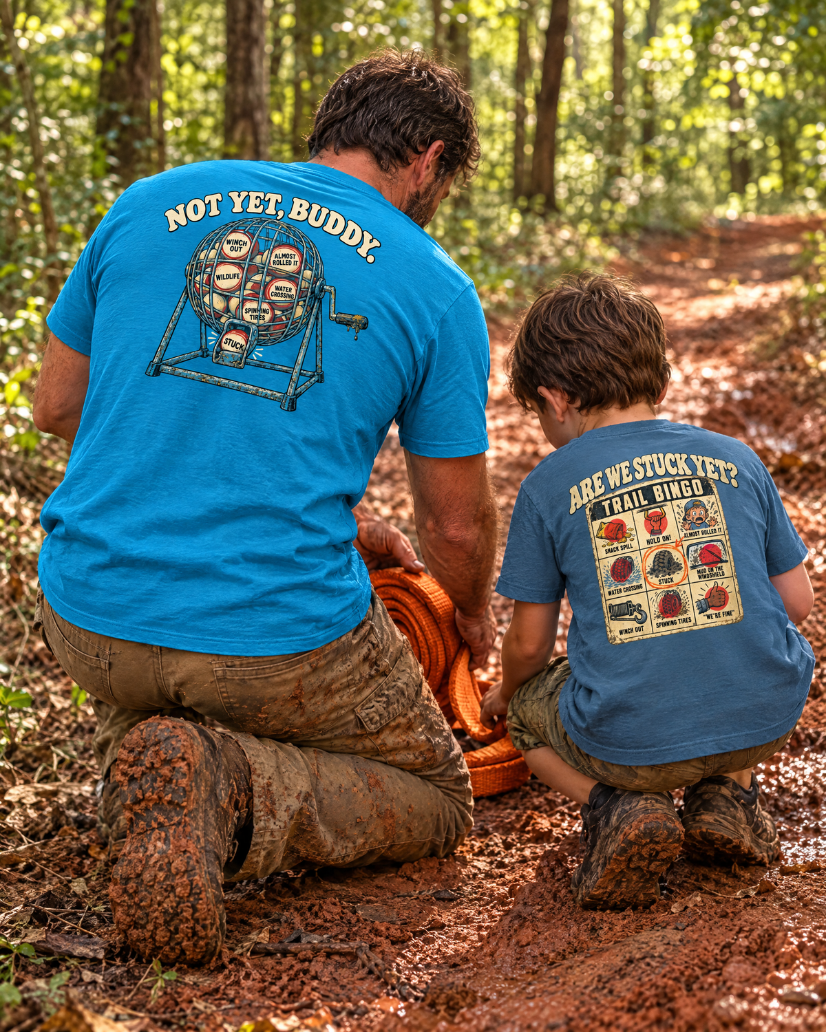 Father and son coiling a recovery strap on a red-clay trail in the matching Are We Stuck Yet? tees