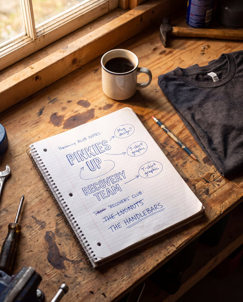 Notebook of handwritten shirt ideas on a garage workbench