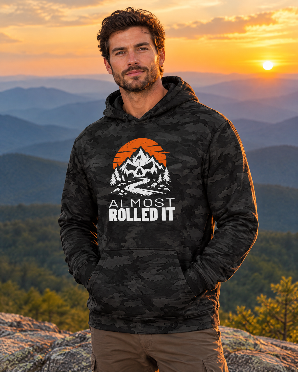 Man wearing the Almost Rolled It Camo Hoodie on a mountain ledge at sunset