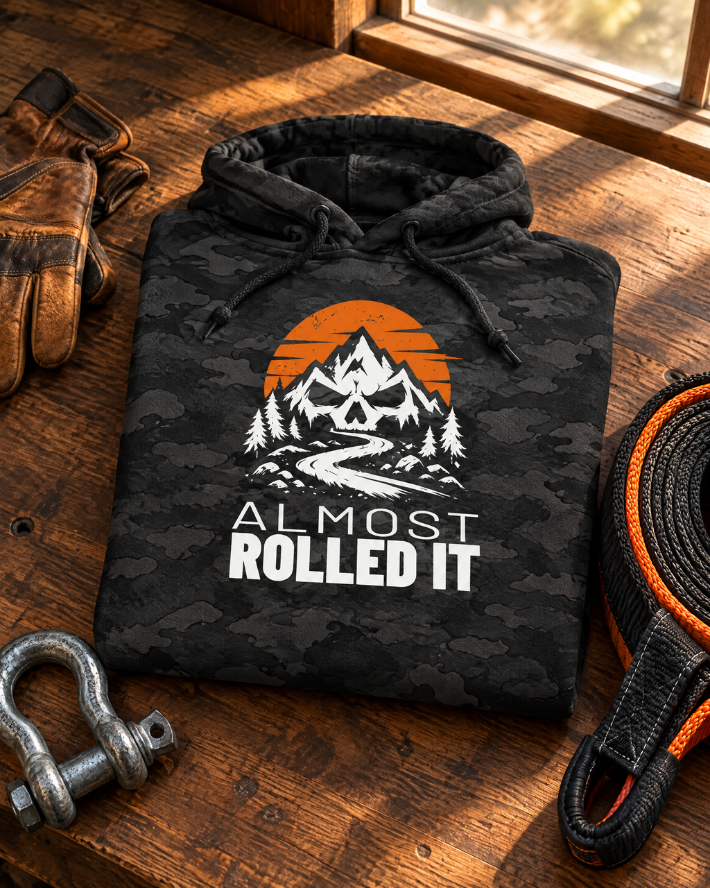Almost Rolled It Camo Hoodie folded on a workbench with gloves, a shackle and a recovery strap