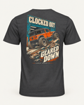 Clocked Out tee in dark grey, back view: cream CLOCKED OUT lettering over a teal garage door, an orange rig rolling out onto rocks, GEARED DOWN below