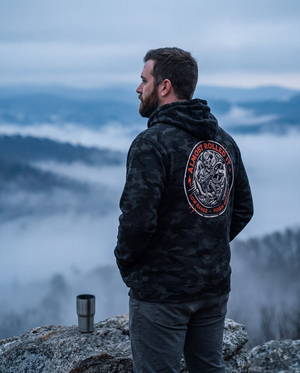Man in the 4Lo Skull camo hoodie on a foggy mountain overlook at dawn
