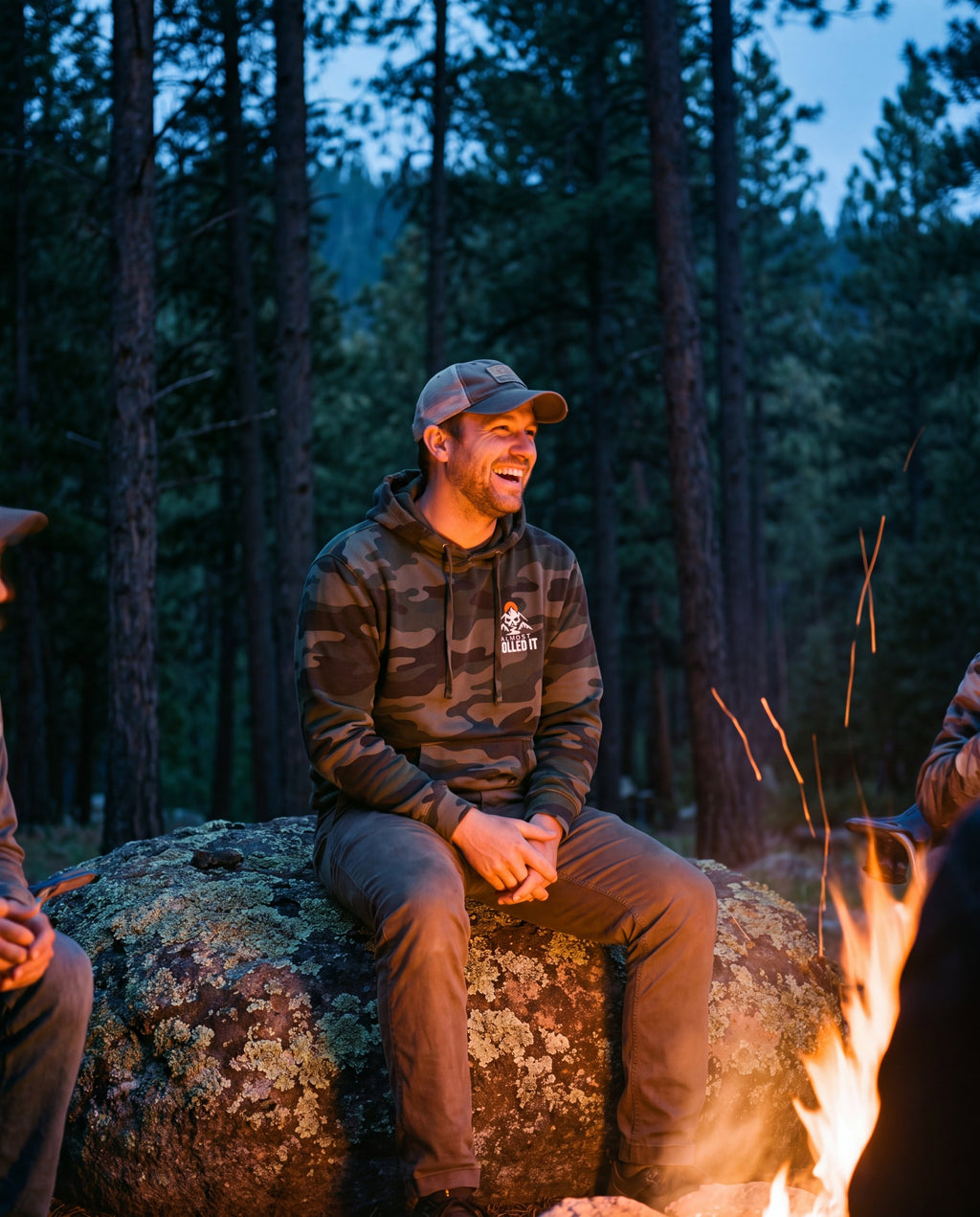 Front of the forest camo Tons & 42s hoodie by a campfire: small chest logo