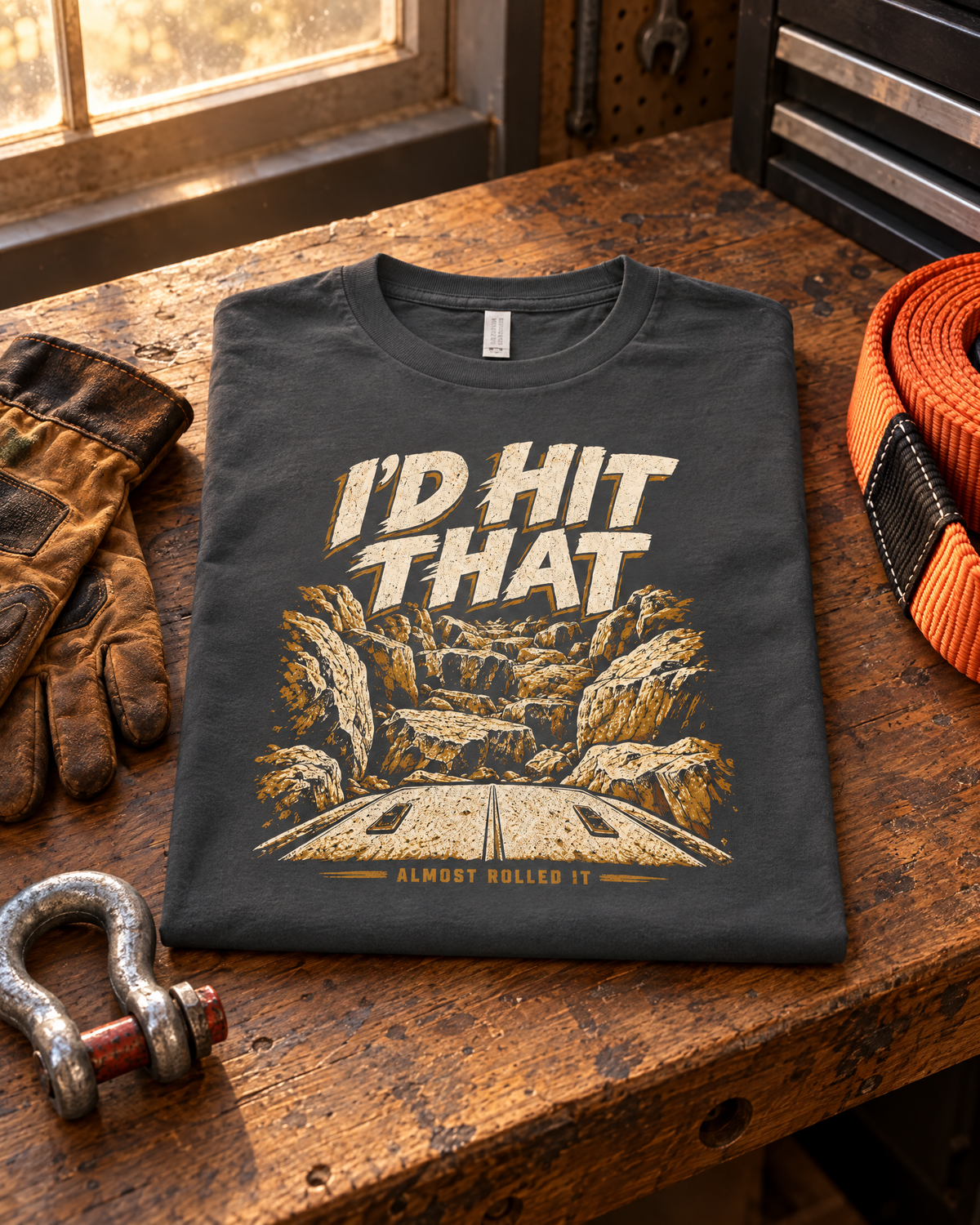Dark grey I'd Hit That tee folded on a walnut workbench with gloves, a shackle and a recovery strap