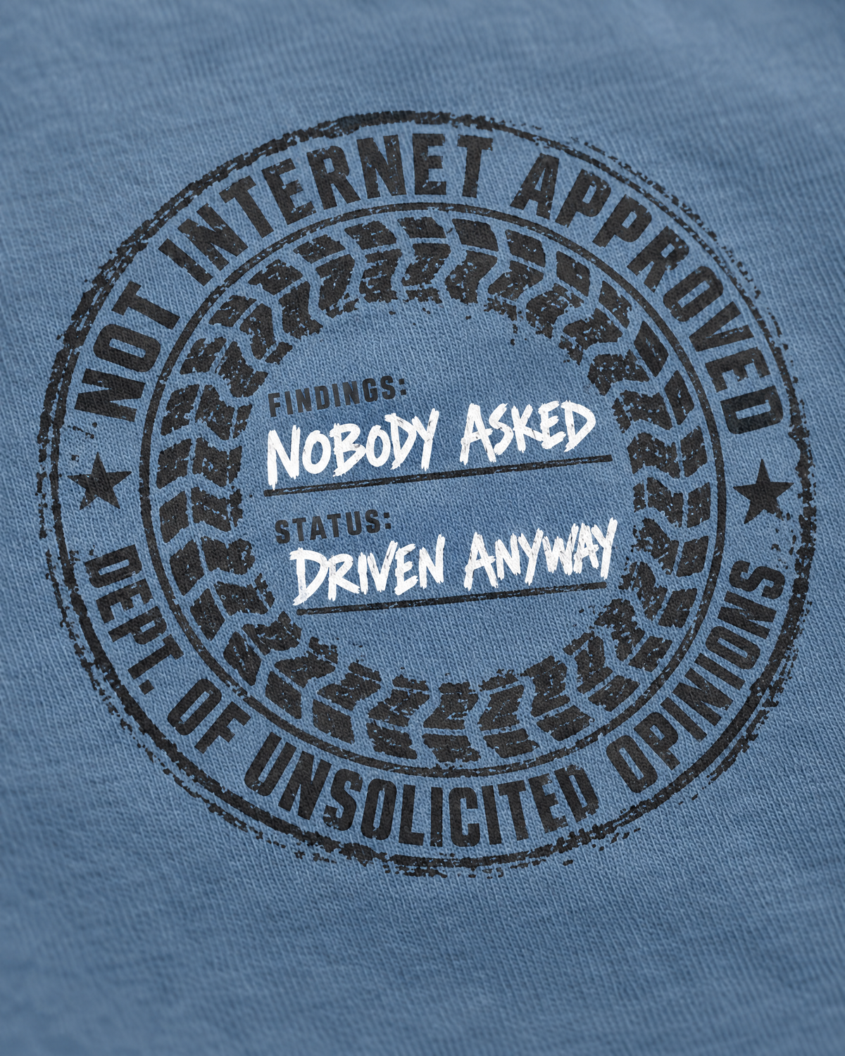 Close-up of the Nobody Asked stamp print: tire-tread ring and white Driven Anyway lettering on slate cotton