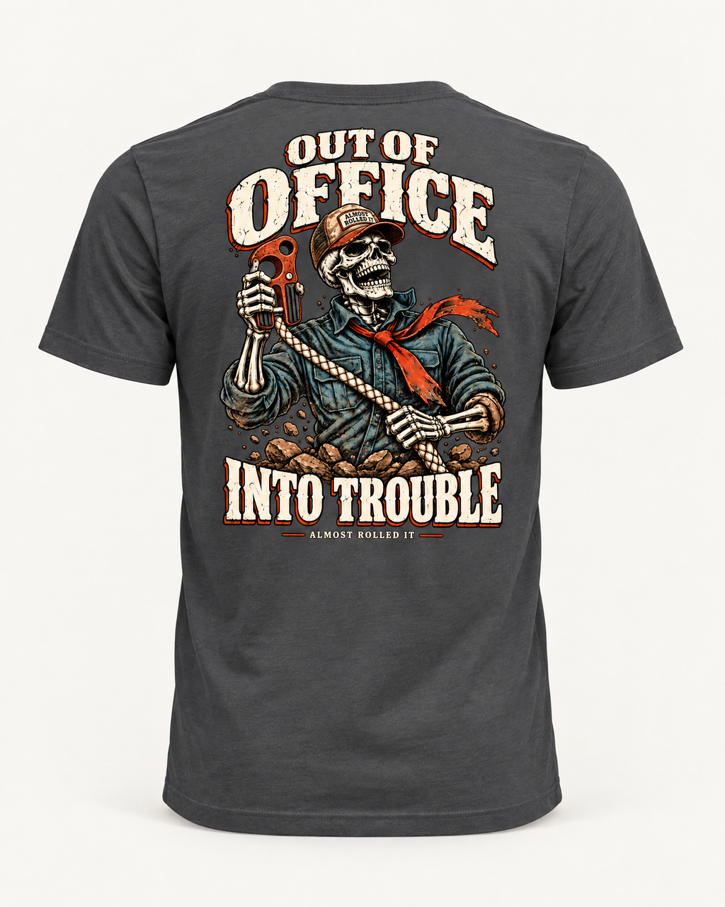 Out of Office tee in dark grey, back view: OUT OF OFFICE, INTO TROUBLE in cream lettering around a laughing skeleton in a trucker cap and red bandana holding a red hook on a rope