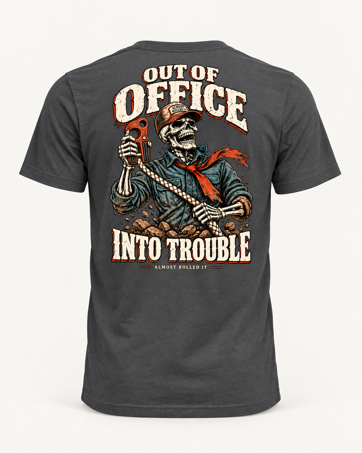 Out of Office tee in dark grey, back view: OUT OF OFFICE, INTO TROUBLE in cream lettering around a laughing skeleton in a trucker cap and red bandana holding a red hook on a rope