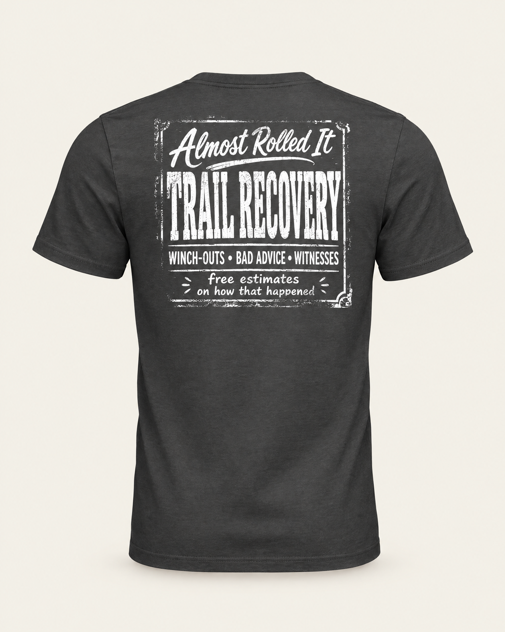 Trail Recovery Badge tee in dark grey, back view: white vintage-sign print reading Almost Rolled It Trail Recovery, winch-outs, bad advice, witnesses