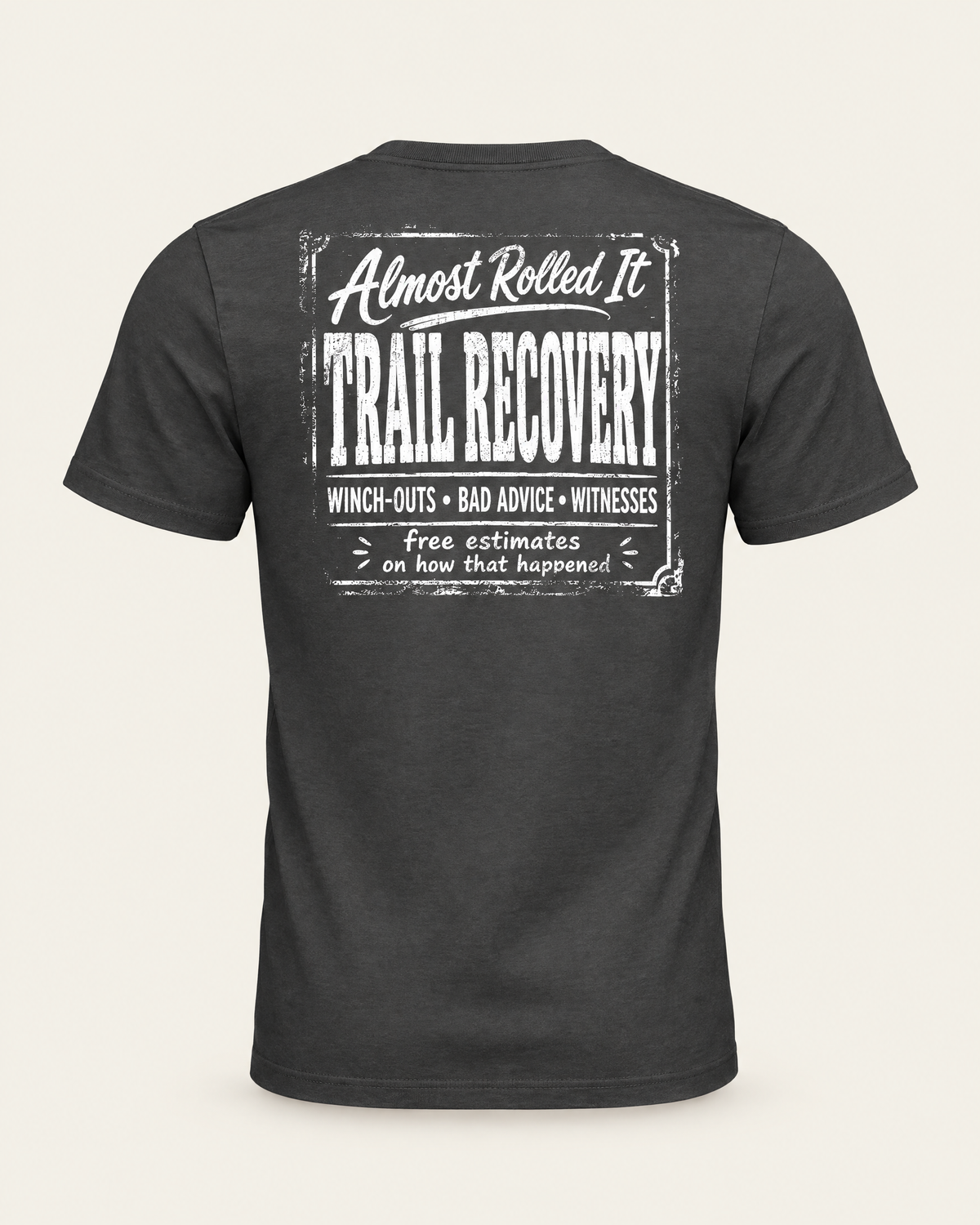 Trail Recovery Badge tee in dark grey, back view: white vintage-sign print reading Almost Rolled It Trail Recovery, winch-outs, bad advice, witnesses