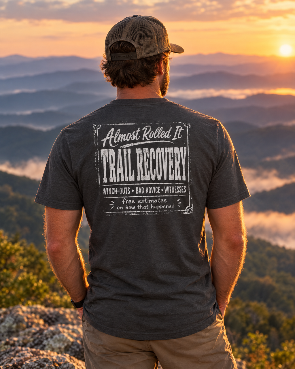 Man wearing the Trail Recovery Badge tee on a mountain ledge at sunset, back print showing
