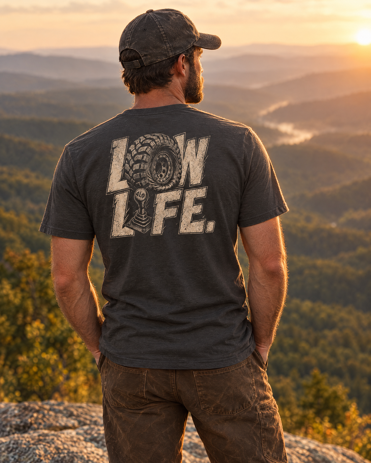 Man wearing the Low Life tee on a mountain ledge at sunset, back print showing