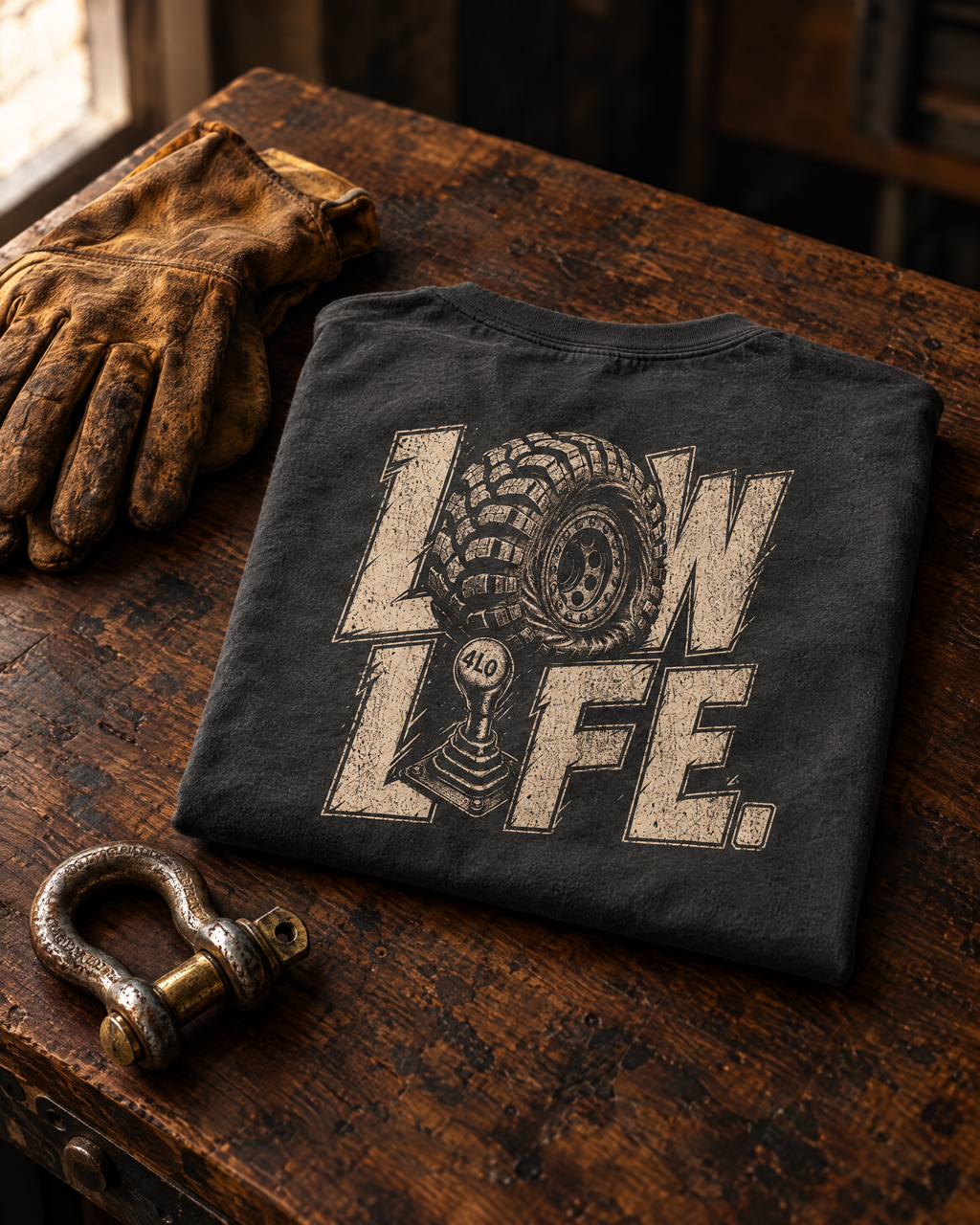 Low Life tee folded on a walnut workbench next to leather gloves and a shackle