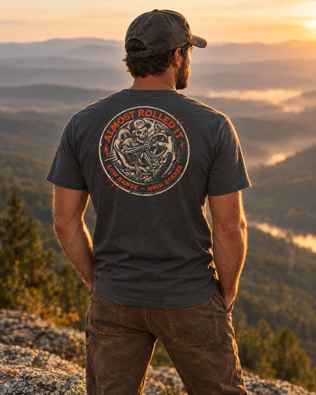 Man wearing the 4Lo Skull tee on a mountain ledge at sunset, back badge showing