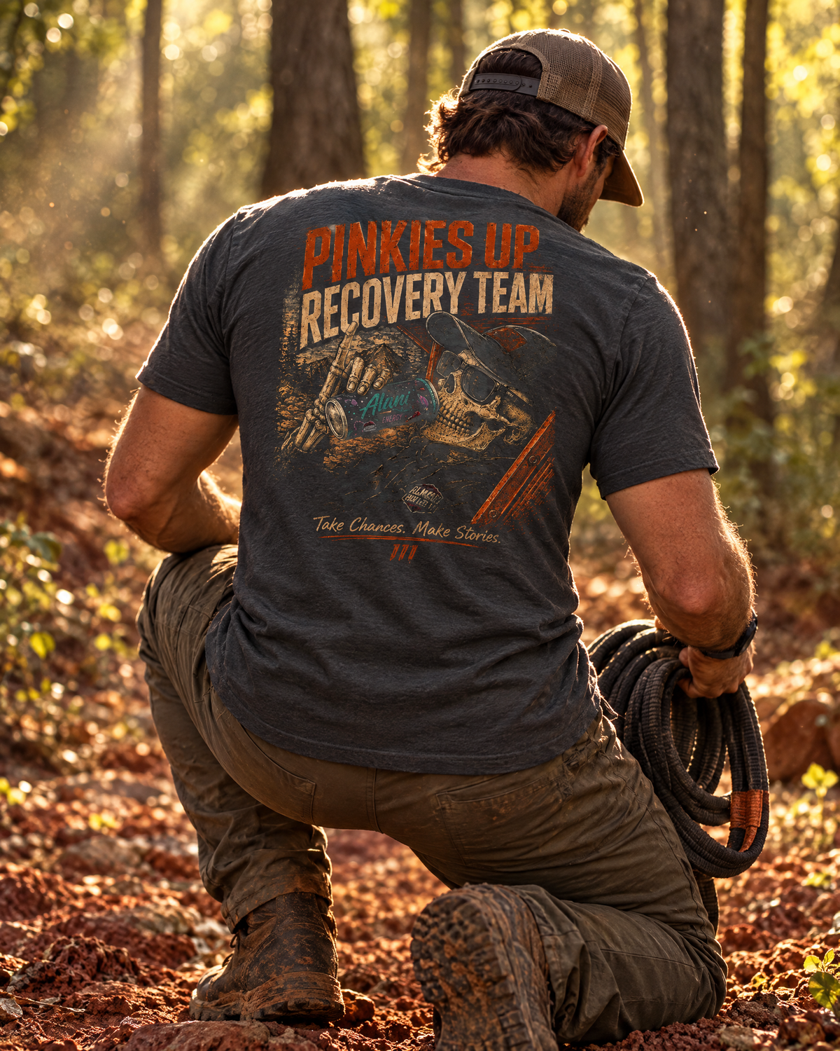 Man coiling a recovery strap on a red-clay trail in the Pinkies Up tee
