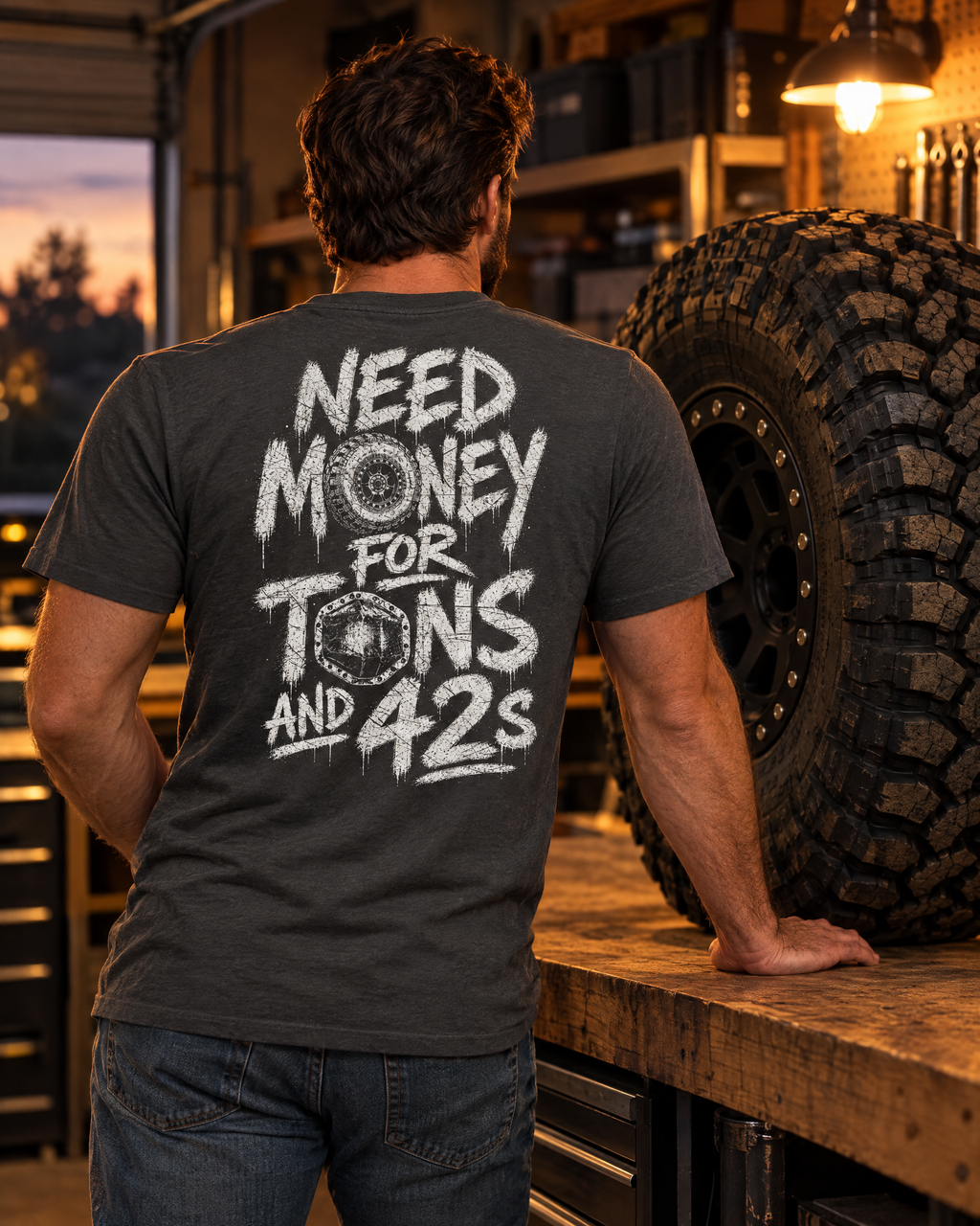 Man in the Tons & 42s tee in a garage next to a 42-inch tire on a beadlock wheel
