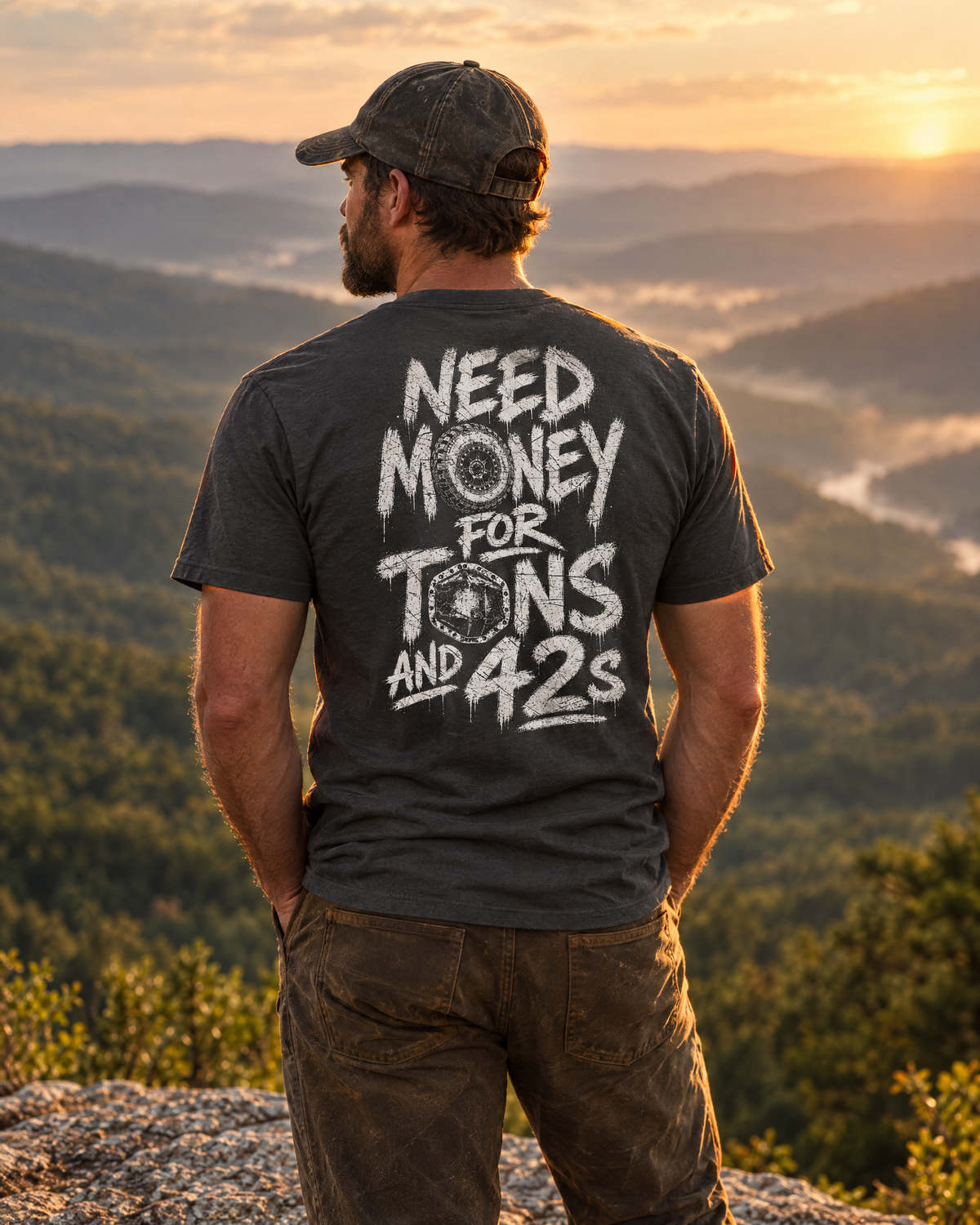 Man wearing the dark grey Tons & 42s tee on a mountain ledge at sunset, back print showing