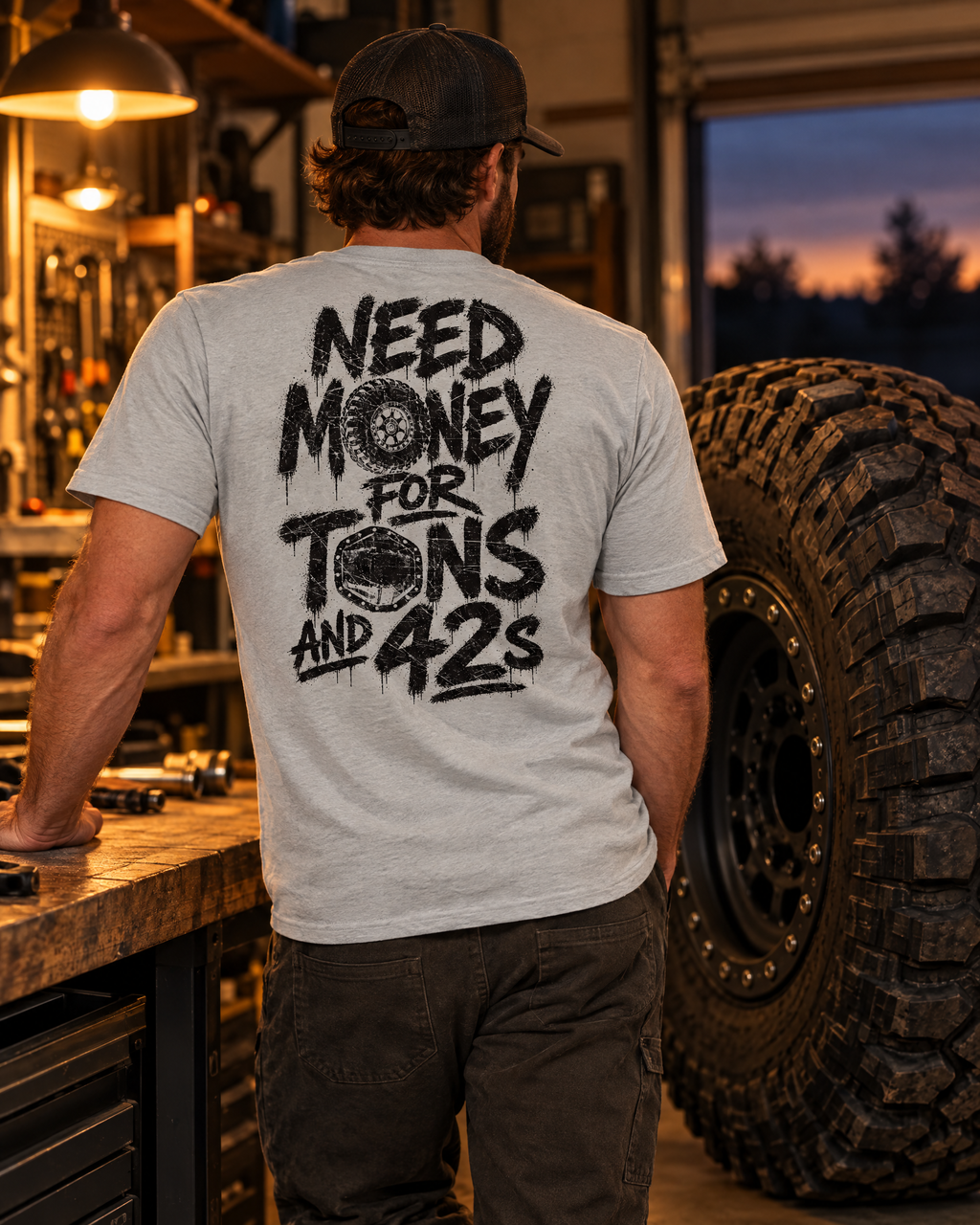 Man in the silver Tons & 42s tee in a garage next to a 42-inch tire on a beadlock wheel