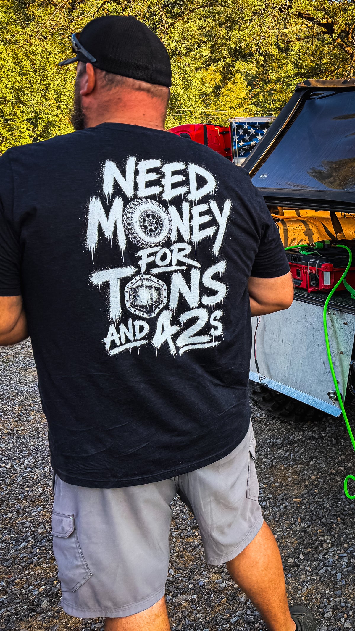Man in the Tons & 42s tee, back print showing, next to a built rig