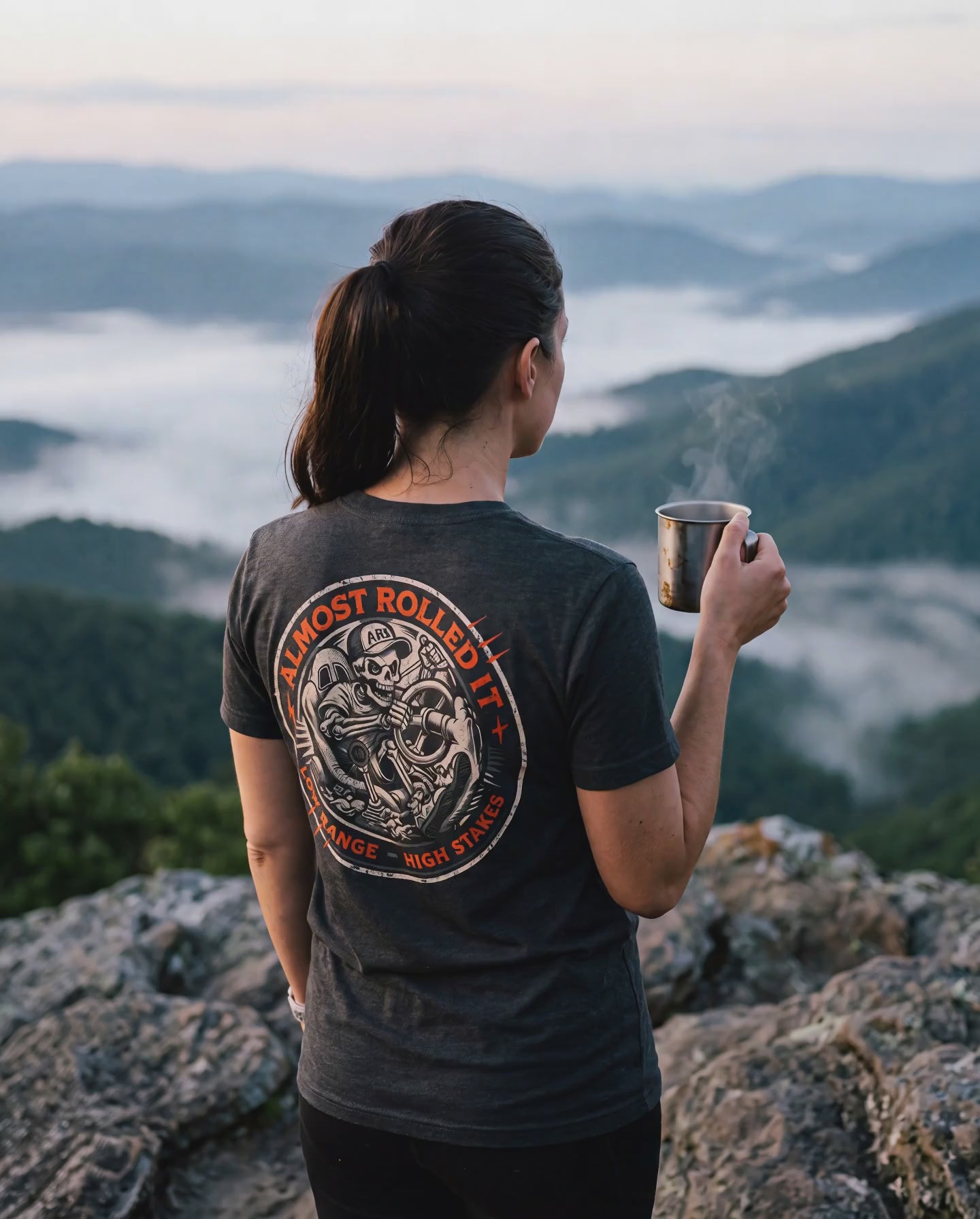 Woman in the 4Lo Skull tee looking out over a foggy ridge, coffee in hand
