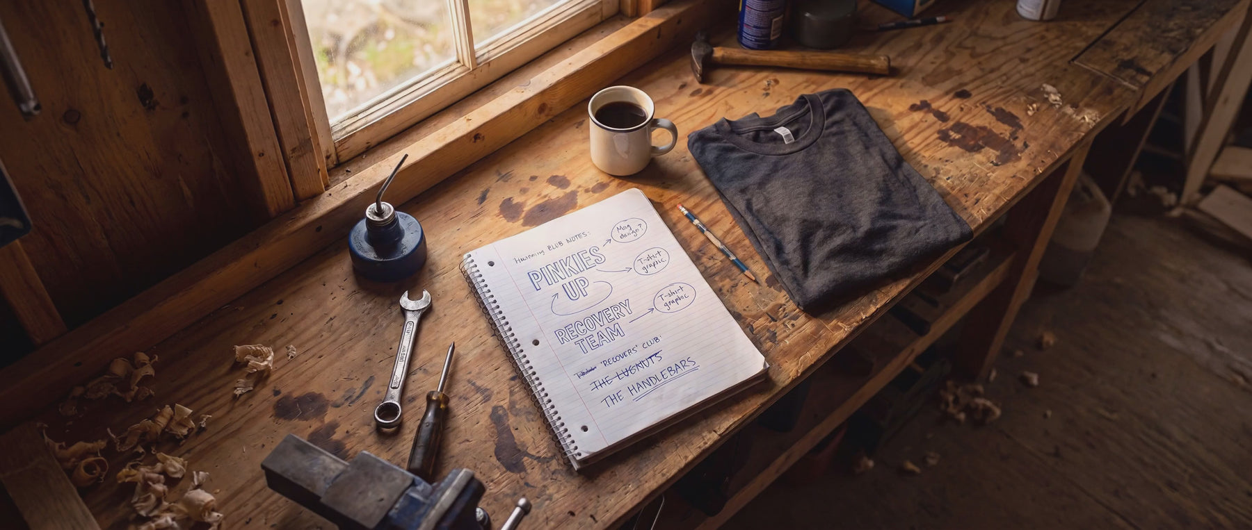 Steam rising from a coffee mug beside a notebook of shirt ideas